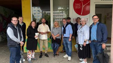 Gruppe von zehn Personen beim Stadtteilspaziergang der FDP Erfurt im Rieth. Sie stehen vor dem Eingang der Tanzschule „Tanz Kreation Erfurt“, lächeln in die Kamera und halten teils Regenschirme in der Hand. Im Hintergrund sind ein gelb gestrichener Gebäudeeingang, Fenster eines Wohnblocks und ein rotes Logo der Tanzschule zu sehen.